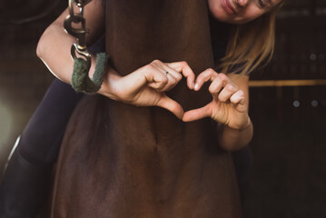 Horsewoman posing with her seal brown horse in the stable. Girl making a heart with her fingers....