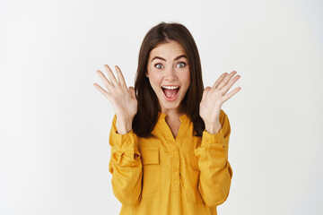 Image of surprised and excited young woman reacting to amazing news, raising hands up and scream of...