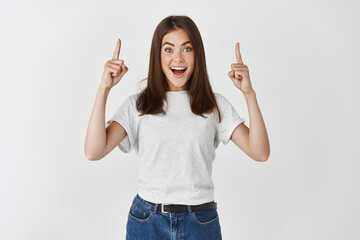 Surprised and happy woman showing advertisement, pointing hands up and looking at camera...