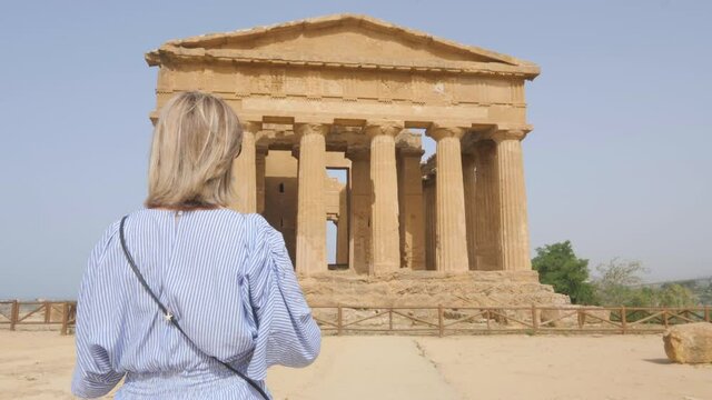 tourist walking to the temple of concordia taking a photo,woman photograph the valley of the temples agrigento sicily italy