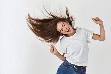 Haircare and beauty concept. Happy young woman dancing and whip healthy shiny hair, having fun, standing joyful over white background