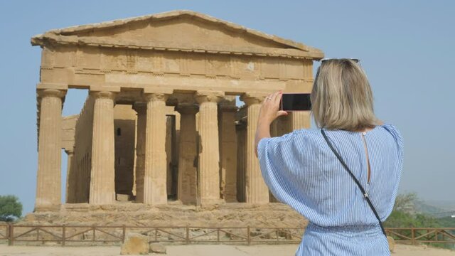 tourist woman photographing temple of concordia,traveller taking picture of the valley of the temples agrigento sicily italy