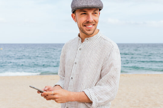 Cheerful man with smartphone on sandy beach