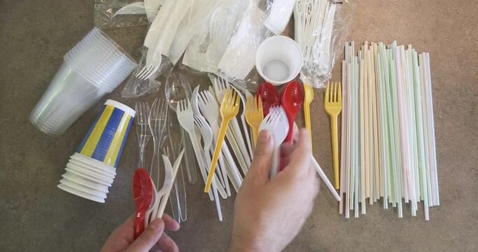 Hand adds plastic cutlery on table with single use plastic items banned in the European Union: straws, cutlery, cups, stirrers.