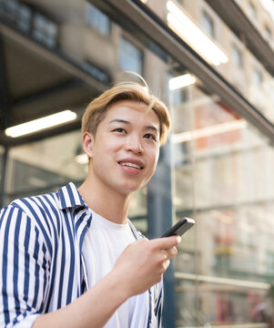Cheerful Asian Man Using Smartphone In City