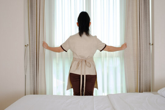 Young maid opening curtains in hotel room
