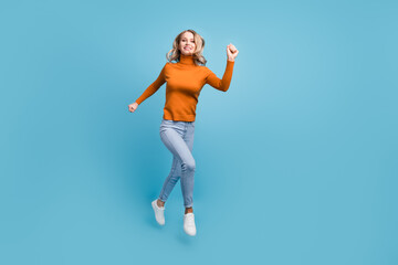 Fototapeta na wymiar Photo of excited cute young woman dressed orange pullover smiling jumping running fast isolated blue color background