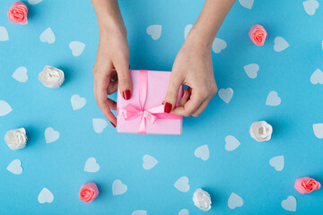 female hands with a gift box on a pastel colored background top view, the girl opening a present and untying a ribbon bow, the concept of holidays and love