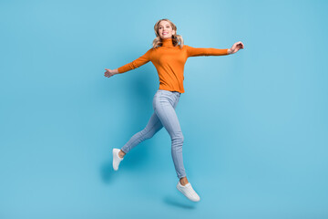 Fototapeta na wymiar Photo of charming shiny young woman dressed orange pullover smiling jumping high isolated blue color background
