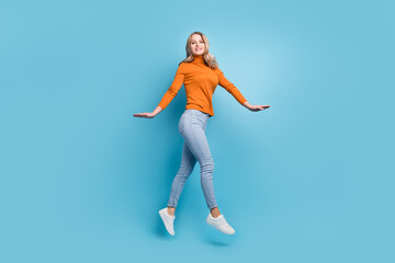 Fototapeta na wymiar Photo of sweet charming young woman dressed orange pullover smiling jumping high walking isolated blue color background