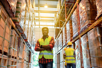 Portrait of black male worker team working in factory warehouse. Black man worker smiling with crossed arms indoor of building in background shelves with goods.Logistic industry concept.