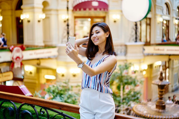 Pretty millennial user smiling at front smartphone camera while shooting video content for sharing to social networks enjoying travel trip during summertime, happy blogger making selfie photos