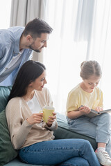 girl reading book near father and mother with cup of tea