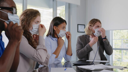 Business people in face mask sitting at desk during corporate meeting in modern office.