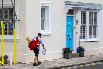 A postman or mail man carrying a mail bag delivering post to english homes - obrazy, fototapety, plakaty