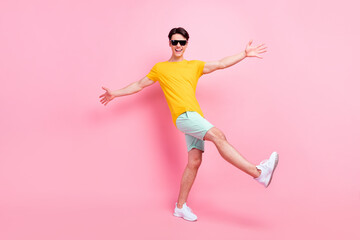 Fototapeta na wymiar Photo of attractive funky young man wear yellow t-shirt dark eyewear smiling walking dancing isolated pink color background