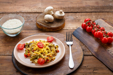 Risotto with bends and cheese in a plate on a wooden background on a round stand next to rice mushrooms and tomatoes on planks.