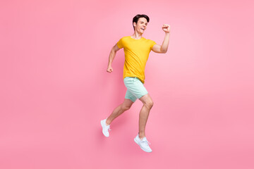 Fototapeta na wymiar Profile photo of cheerful active guy jump run fast hurry rush wear yellow t-shirt shorts footwear isolated on pink background