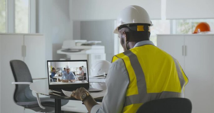 Back view of afro-american male engineer having video chat with foreman on laptop in office
