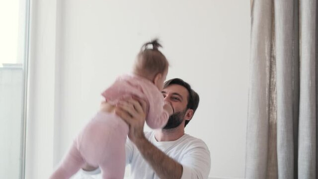 A happy father is throwing up his small daughter at the bedroom