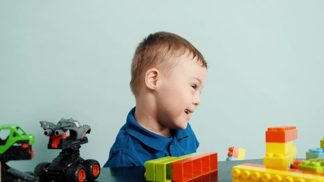A happy little child with down syndrome playing with cars and constructor on the table in the blue studio