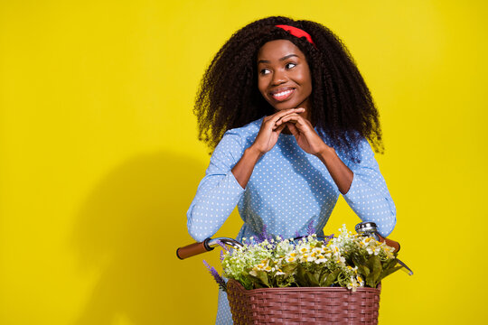 Photo of young positive dark skin woman look empty space ride bike smile enjoy isolated on yellow color background