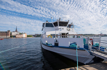 Fototapeta premium Commuting boat at the pier of the Stockholm Town City Hall and the old town Gamla Stan in Stockholm at sunset a summer day.