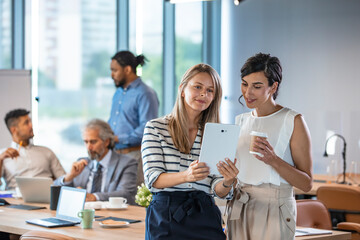 Two colleages discussing ideas using a tablet and computer. Cropped shot of colleagues working together on a digital tablet in a modern office. Businesswomen using digital tablet in office