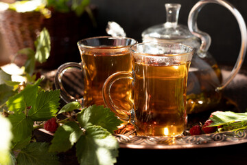 tea is poured into glass mugs. A teapot and a cup of tea stand on a copper tray next to raspberry leaves and berries