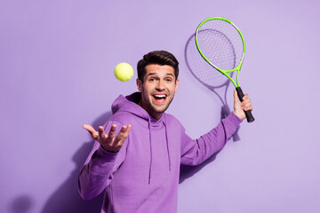 Portrait of attractive cheerful guy playing active tennis having fun isolated over purple violet...