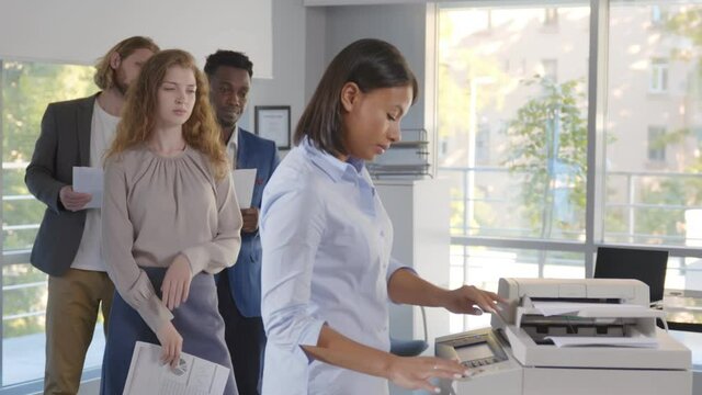 Group of young managers standing in queue for copier at office
