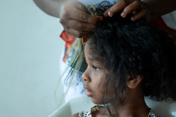 Close up African hairstylist braided hair of afro little girl, mother spend time with girl child...