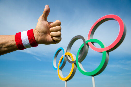 RIO DE JANEIRO - MAY 4, 2016: Japanese athlete's hand wearing red and white  wristband gives a thumbs-up gesture in front of Olympic Rings standing under bright blue sky.