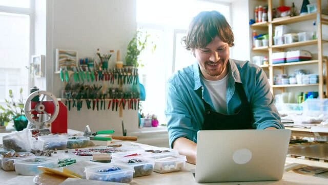 Smiling man typing on laptop in workshop
