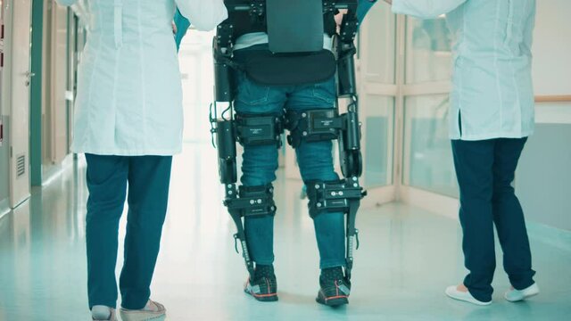 A man in the exoskeleton and doctors are walking along the hall