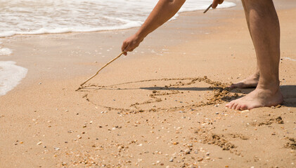 a man's hand draws something on the sea sand with a stick