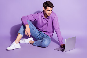 Portrait of attractive cheerful guy sitting using laptop watching tutorial isolated over purple violet color background