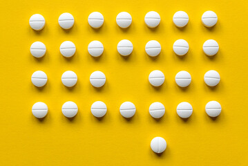 A row of white medical pills on yellow background with one missing spot in the middle and one pill outside the row.