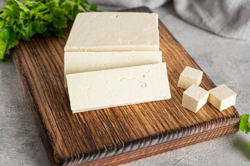 Fresh cheese tofu from soybeans with parsley on a board on a gray concrete background. A vegan product. Copy space.
