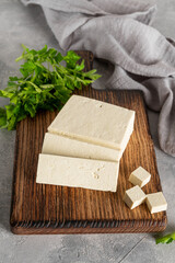 Fresh cheese tofu from soybeans with parsley on a board on a gray concrete background. A vegan product. Copy space.