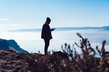 Anonymous man on mountain top browsing cellphone