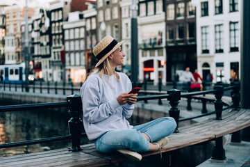 Smiling woman with smartphone sitting on bench - obrazy, fototapety, plakaty
