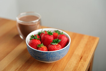 strawberries in a bowl and cocoa in a glass on a wooden table