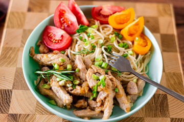 Fried meat and spaghetti on a plate on a wooden background with tomatoes and herbs.