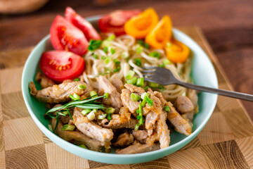 Fried meat and spaghetti on a plate on a wooden background with tomatoes and herbs.