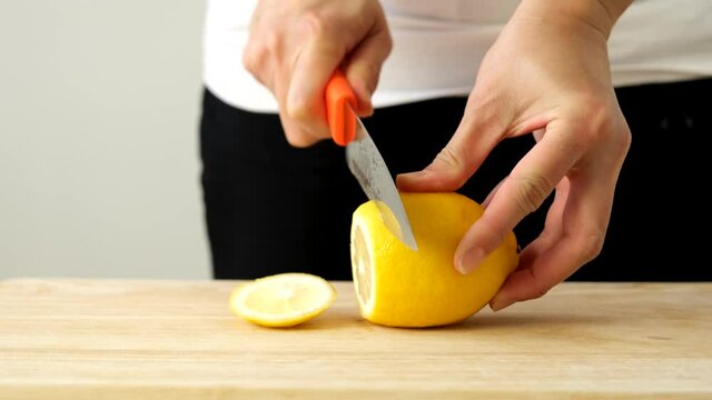 A woman's hand is using a knife to slice a thin lemon to marinate honey and lemon.