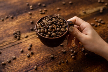 Coffee beans full cup and female hands on brown old wooden background.