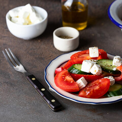 Vegetable salad made from   cucumber, tomato, sweet pepper  and feta cheese, dressing with olive oil in the white blue plate ontable table