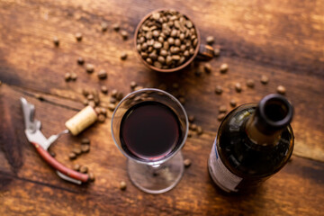 Glass with red wine and coffee beans on a brown old wooden background.