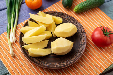 Tubers of raw peeled cut potatoes on a plate on the kitchen table with vegetables. Preparation for cooking.